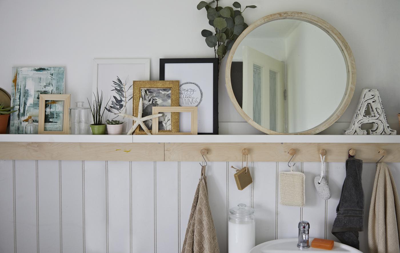 Miroir, plantes, illustrations et coquillages sur une tablette de salle de bain placée au-dessus de crochets.
