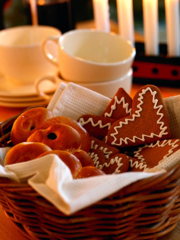Miska perníčků a kynutého pečiva lussekatt, za nimi stojí zapálené svíčky.