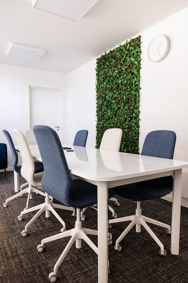 Modern conference room with white table, swivel chairs, and vertical green wall.
