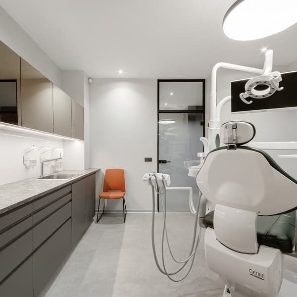 Modern dental clinic interior with green dentist chair, overhead light, and sleek cabinets, featuring an orange chair in the corner.