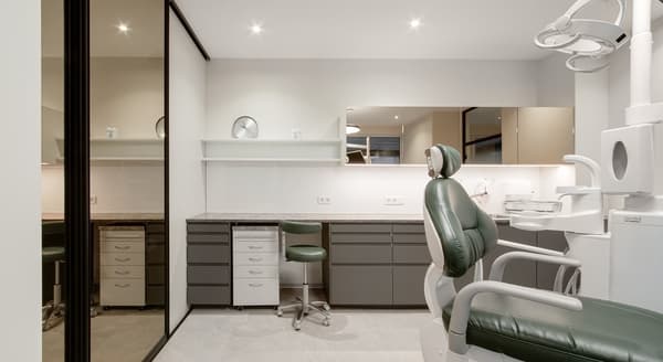 Modern dental clinic interior with green dentist chair, white walls, sleek cabinets, and professional lighting.