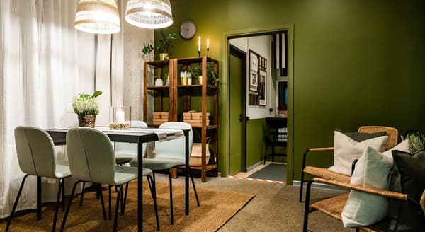 Modern dining room with green walls, wooden shelving, and minimalist table set with plants