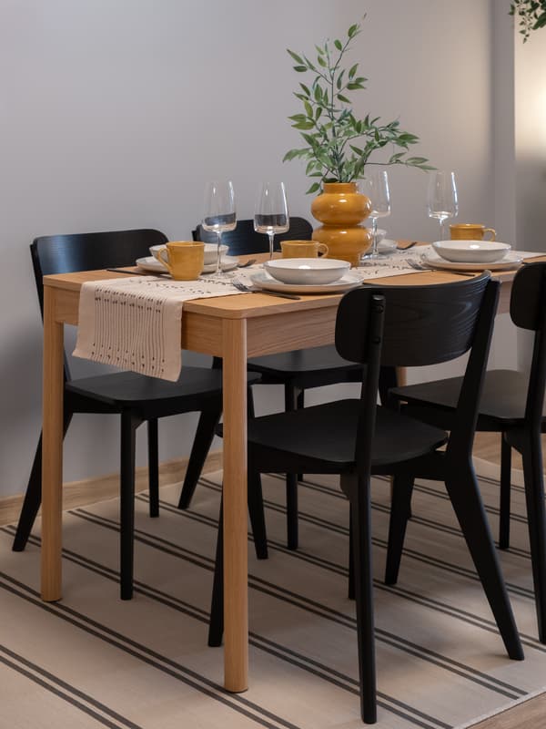 Modern dining setup with a wooden table, black chairs, neutral tableware, and warm ambient lighting.