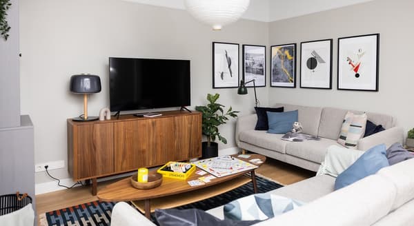 Modern living room with grey sofas, wooden TV cabinet, wall art, and Monopoly board game on coffee table.