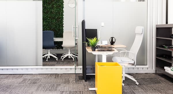 Modern open office with ergonomic desk setup, glass partition, and green wall accent.