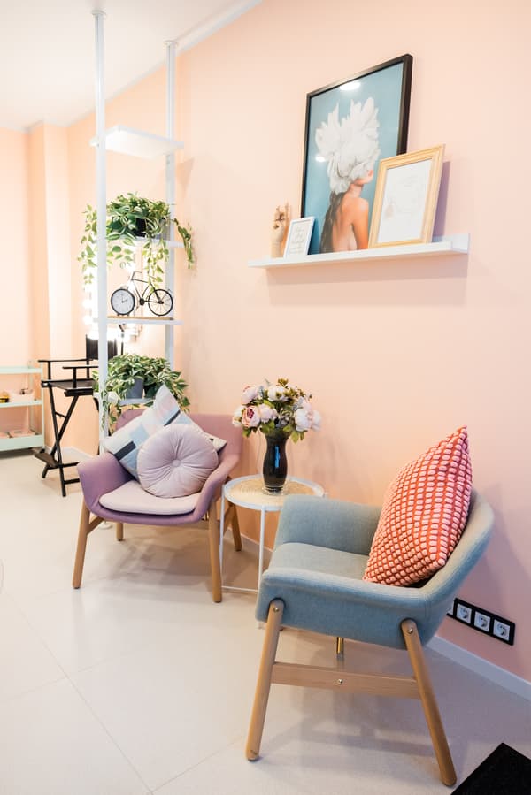 Modern salon seating corner with pastel chairs, cushions, and fresh flowers on a small table.