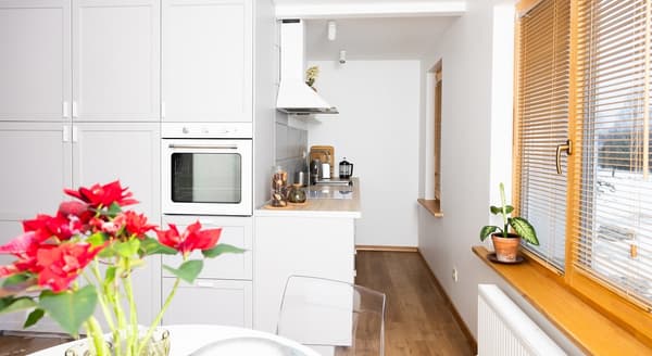 Modern white kitchen with built-in oven, wooden countertop, and window with blinds.