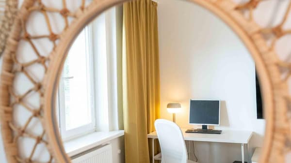 Moderní kancelářský kout v útulném interiéru s dřevěným zrcadlem, bílým stolem a židlí, ideální pro home office nebo studium. Minimalistický design, prosvětlený prostor.