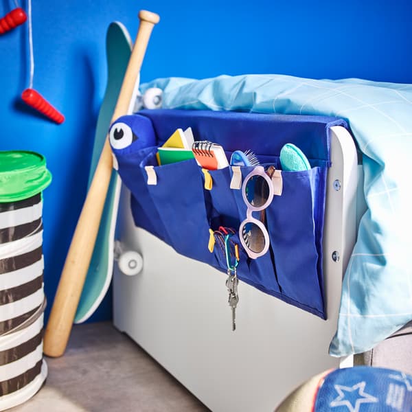MÖJLIGHET bright blue bed pocket with five different sized pockets to place sunglasses, hairbrushes and accessories slung across SLÄKT bed.