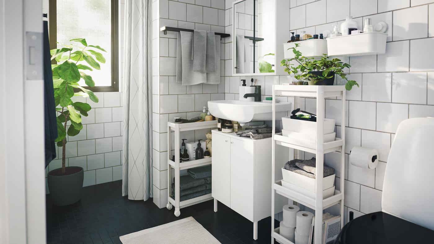 Monochromatic contemporary styled bathroom with several space saving storage units, trolley and indoor green plants.