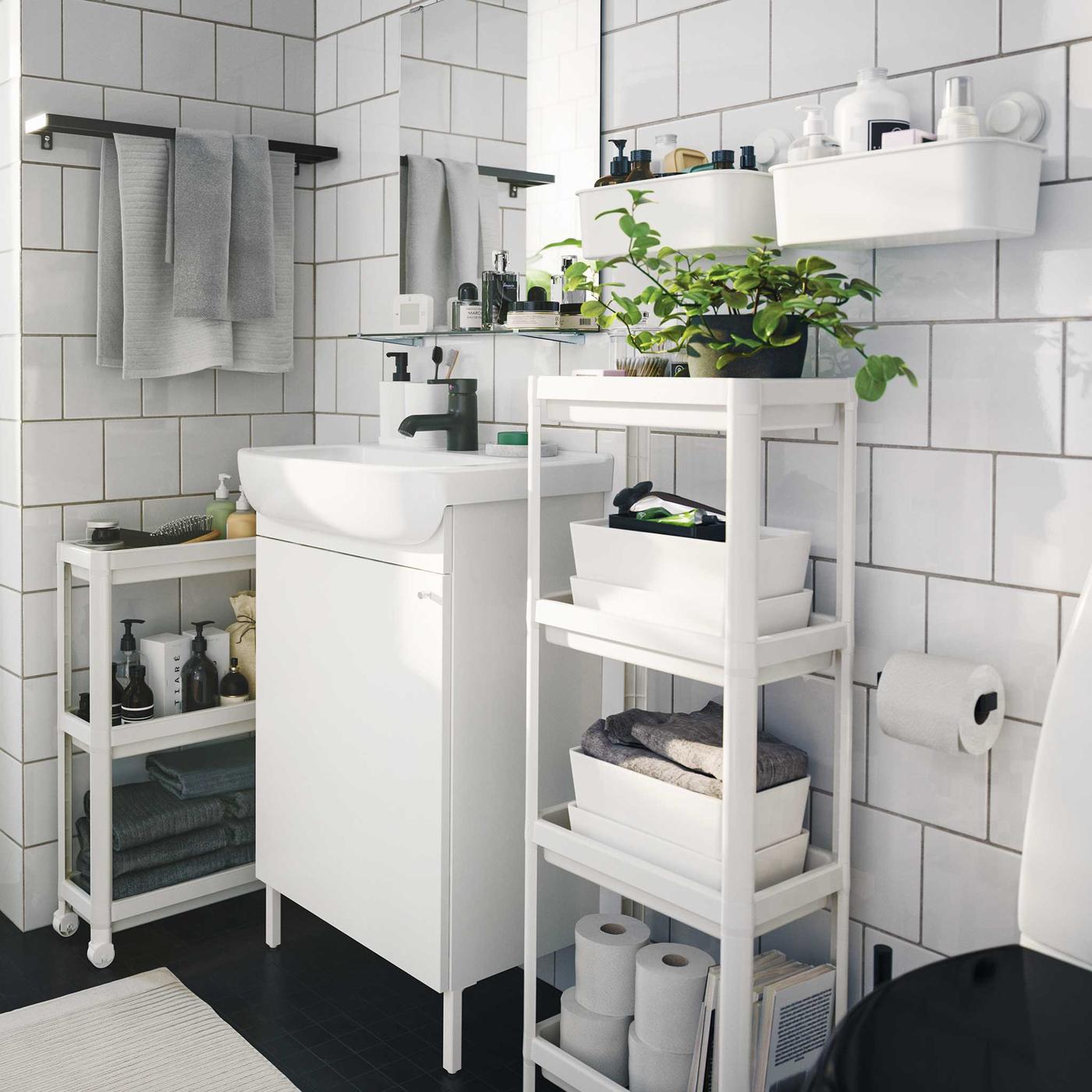 Monochromatic contemporary styled bathroom with several space saving storage units and boxes and indoor green plants.