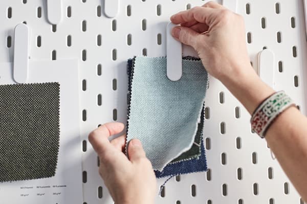 Moodboard with a hand pinning some fabrics at the wall.