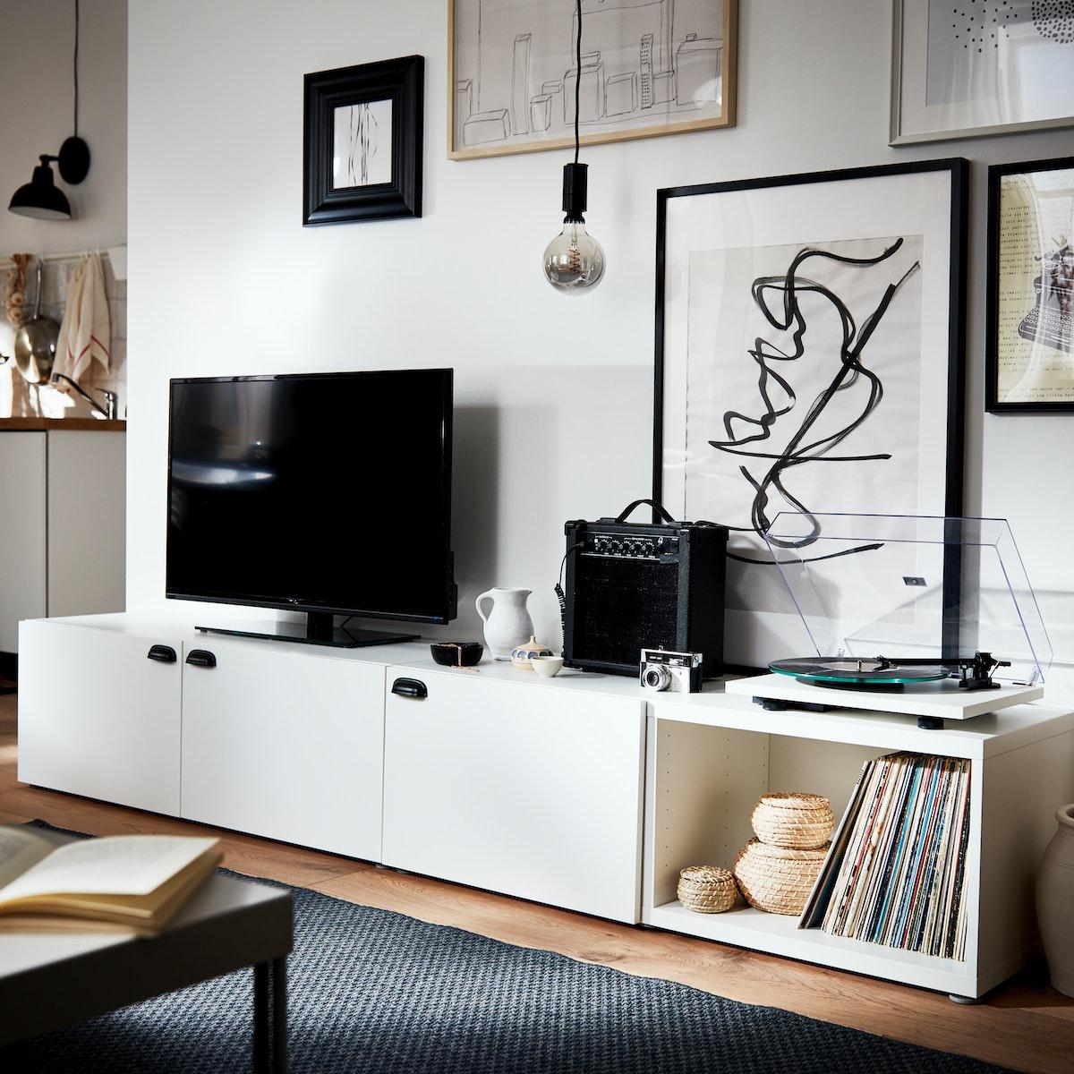 Mueble de la serie BESTA de color blanco, en la pared colgado cuadros y accesorios decorativos.