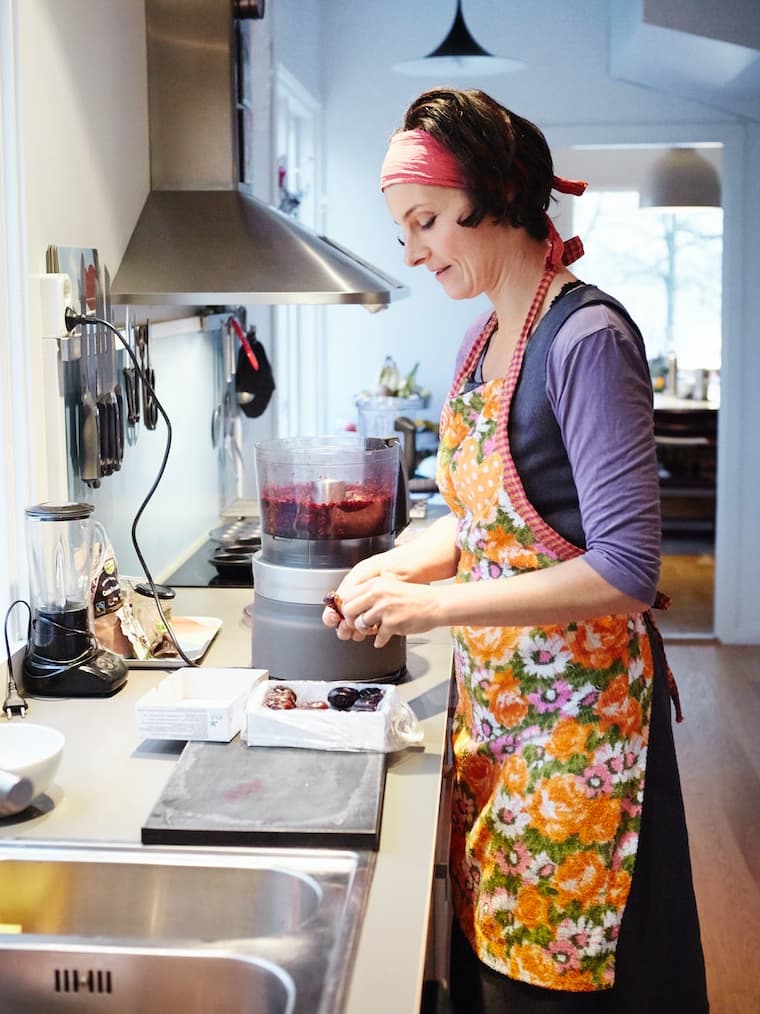Mujer con un delantal de flores color naranjo en la cocina con un cuchillo cortando verduras.