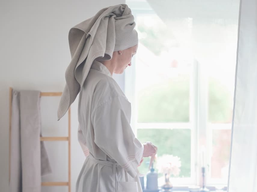 Mujer en un baño con una bata de color blanco y una toalla en la cabeza.