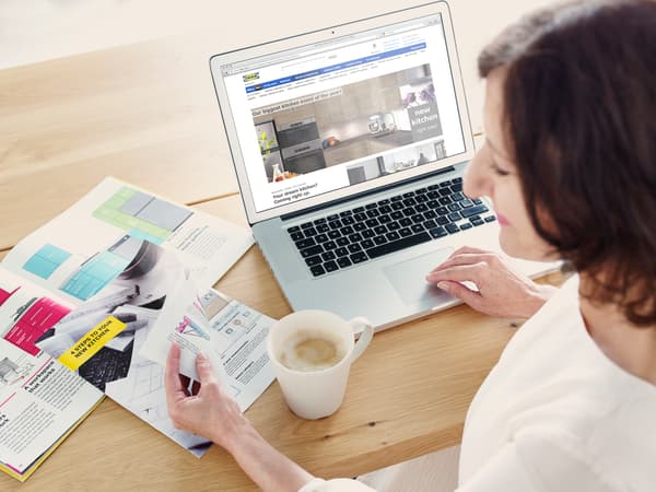 Mujer mirando un computador sobre un escritorio, junto a una revista y una taza de cabeza.