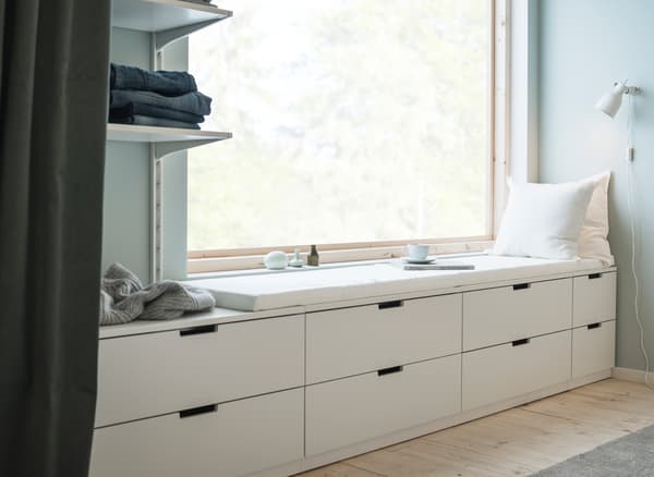 Mur avec fenêtre et rangements bas alignés en dessous, composés de commodes blanches et modernes