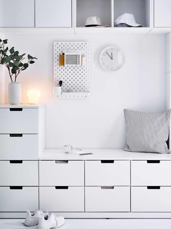 Mur blanc d’une entrée couvert d’une combinaison NORDLI. Un espace central permet de s’asseoir, un panneau perforé SKÅDIS et des objets décoratifs.
