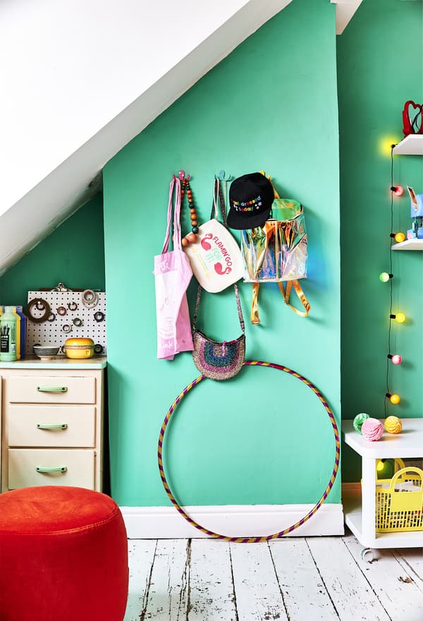Mur vert avec crochets et pouf orange.