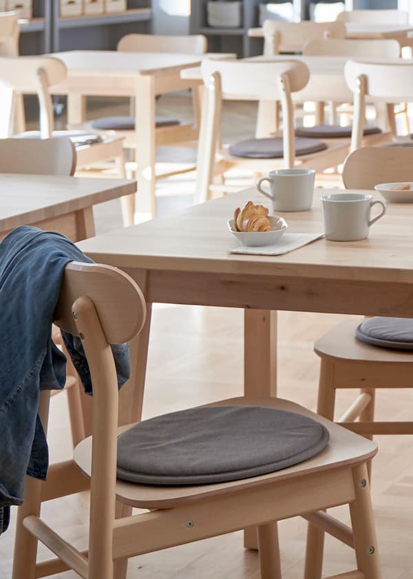 Mysig cafémiljö med LISABO bord och stolar i björk. På bordet står två vita muggar och en tallrik med bakverk.