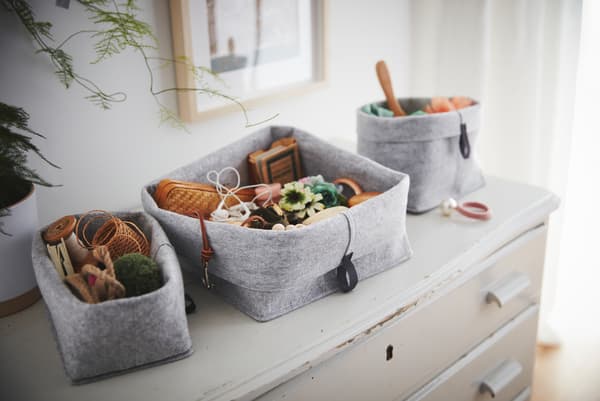 Na starem, obrabljenem predalniku stoji komplet RAGGISAR košar iz blaga, napolnjenih z raznimi drobnarijami.