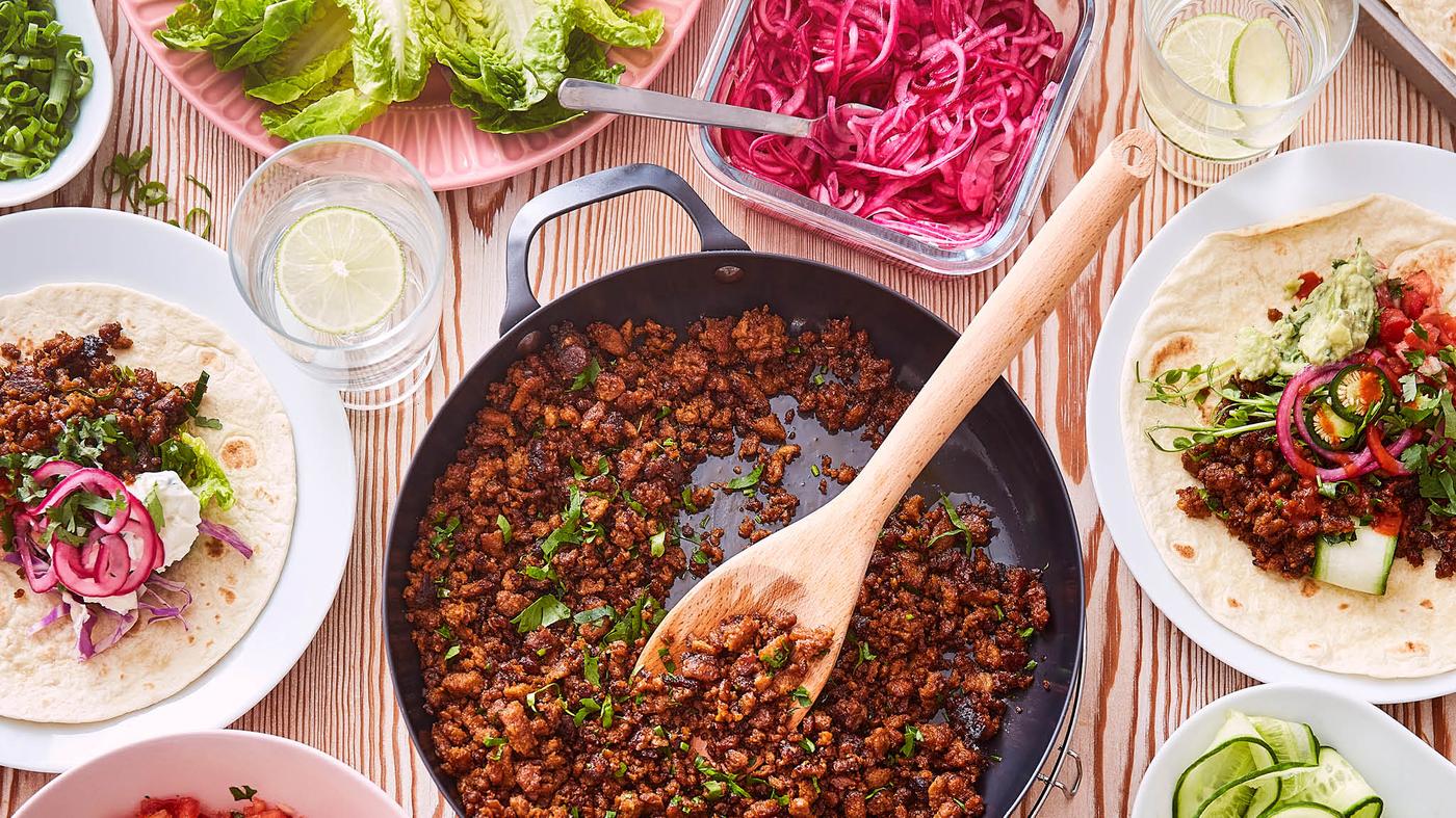 Na stole leží pánev VARDAGEN plná bezmasé směsi VÄRLDSKLOK na Tacos, okolo jsou talíře s tortillami a miska s naloženou červenou cibulí.