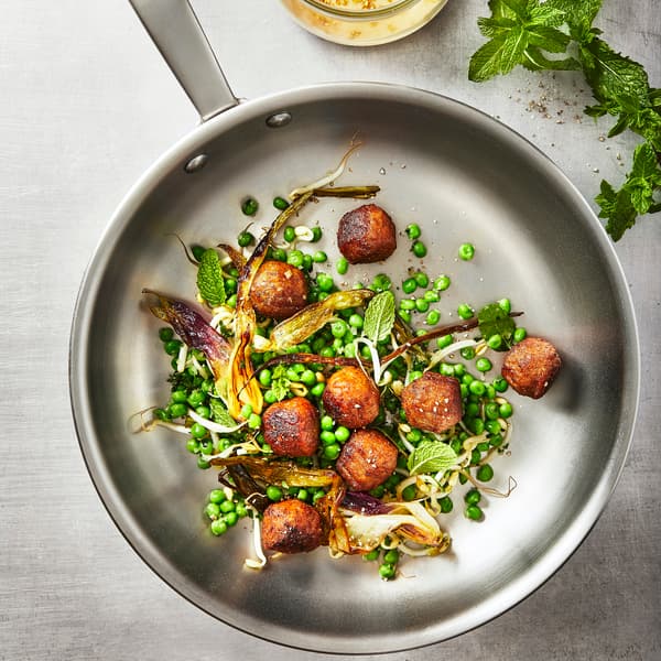 Närbild på stekpanna med åtta köttbullar tillsammans med ärtor och stekt kål.