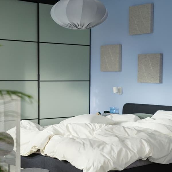 NÄVERHÄGG geluidsabsorberende panelen aan een blauwe muur boven een onopgemaakt bed.
