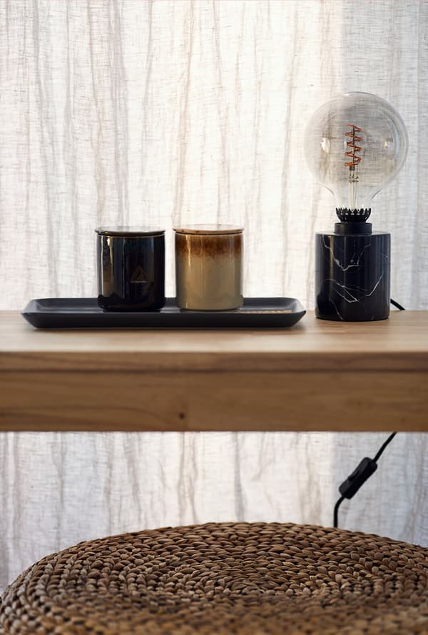 Nahaufnahme eines Holztisches mit Duftkerzen und einer Tischlampe mit Marmorfuss