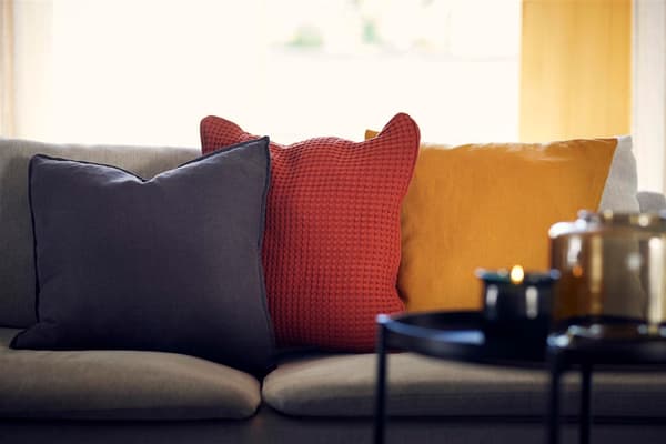 Nahaufnahme von drei einfarbigen Kissen aus unterschiedlichen Stoffen und auf einem Sofa