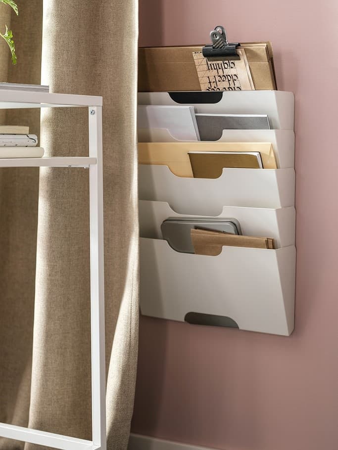 Nástěnný pořadač IKEA KVISSLE s několika přihrádkami na dokumenty a dopisy, namontovaný na růžové stěně vedle stolu.