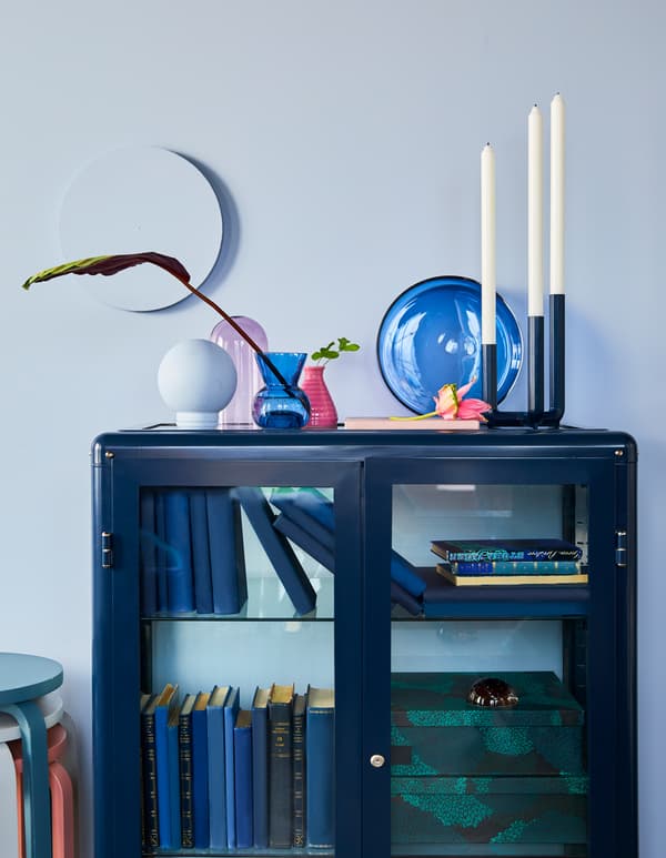 Nature morte décorative composée de vases, de plats et de globes en verre coloré, placés sur le dessus d’une armoire bleu foncé, le tout de chez IKEA.
