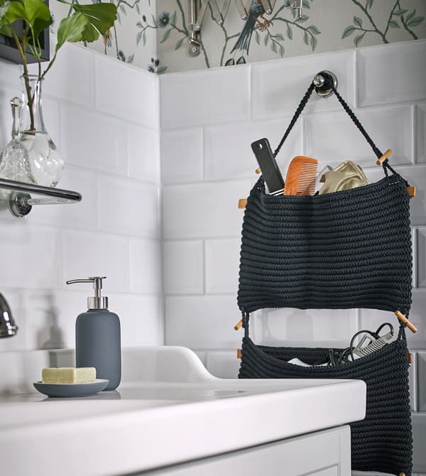 Navy NORDRANA hanging storage filled with bathroom essentials, hung on a white tile wall.