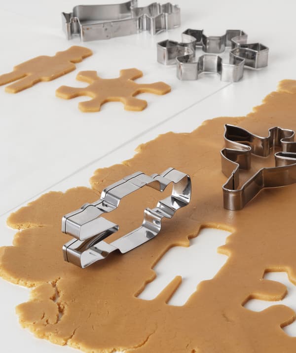 Neatly rolled gingerbread dough on table; various pastry cutters involved in the process of cutting out shapes.
