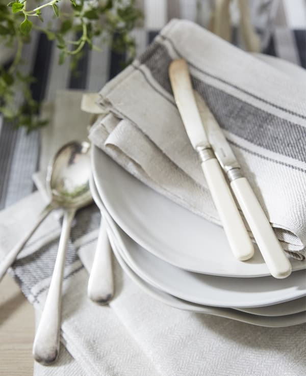 Neutral-coloured cotton napkins and cutlery on a stack of white plates.