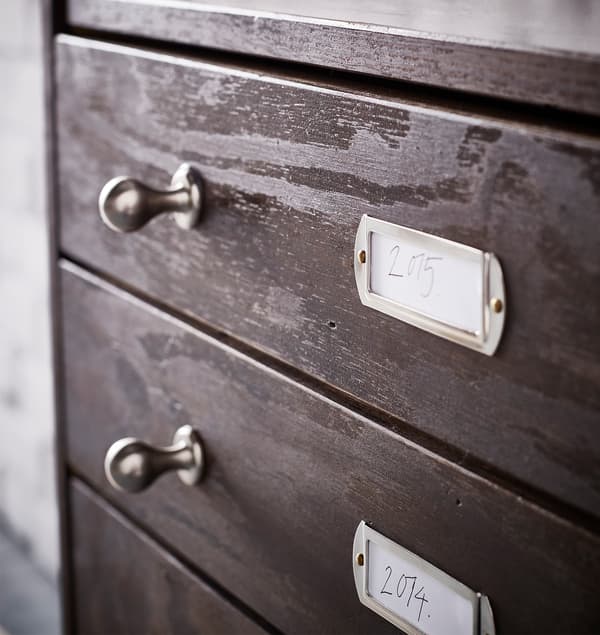 New metal knobs and label plates on an IKEA RAST 3 wooden drawer chest in stained dark brown.