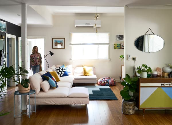 Nici entering a white living room with large pale pink sofa, blue rug and vintage sideboard.