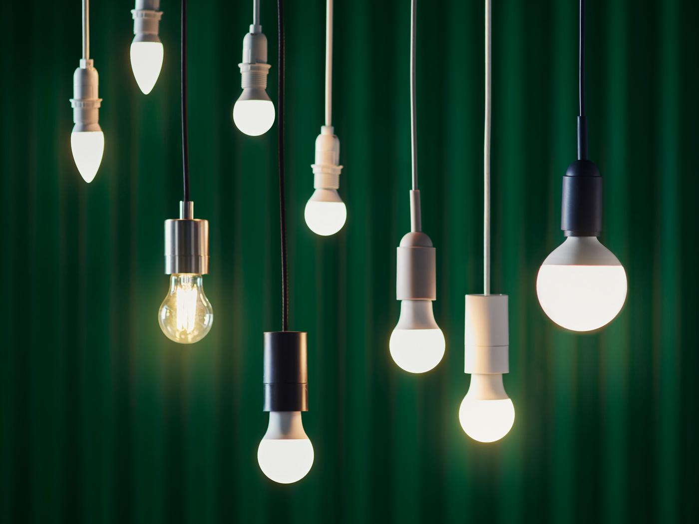 Nine LED bulbs in various designs hung at different heights against the backdrop of a dark green curtain.