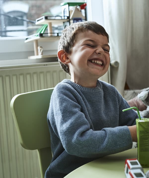 Noah ابن Amélie يجلس ضاحكًا على طاولة.