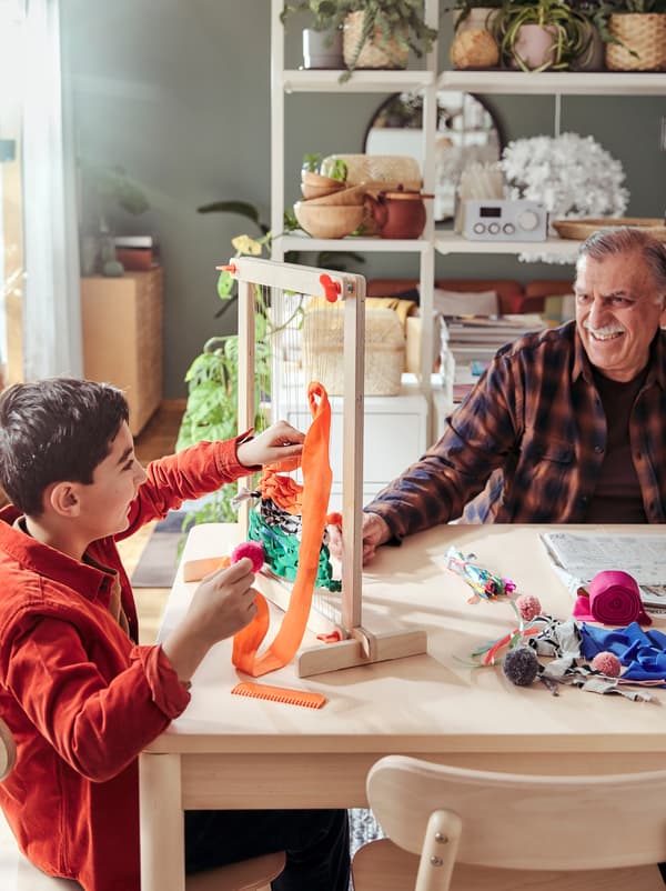 Nonno e nipote seduti al tavolo, giocano insieme con un set telaio LUSTIGT.
