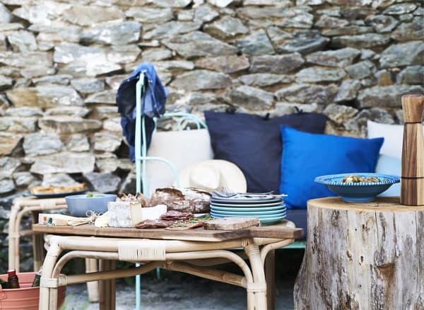 Nourriture servie sur des planches en bois posées sur une table basse et siège garni de coussins bleus adossé à un vieux mur en pierre.