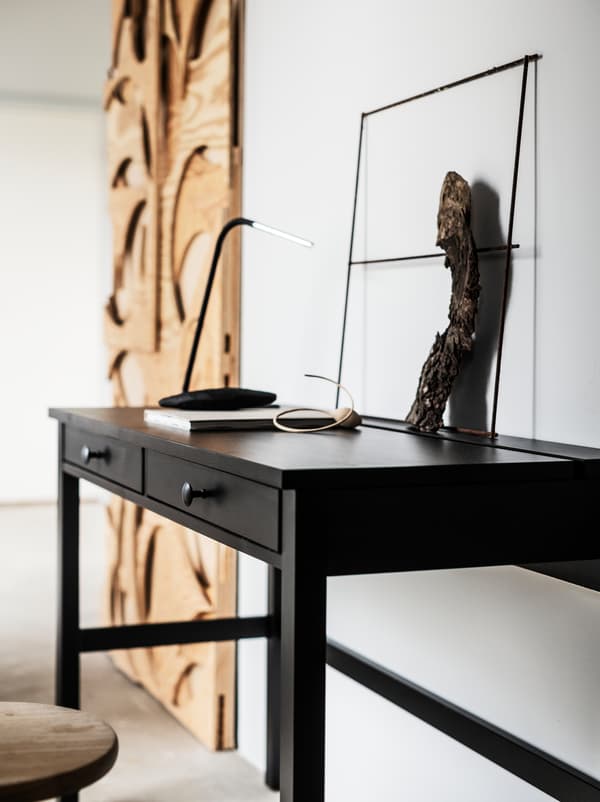 Objects made of light, untreated wood placed along a wall in a white room, one of them a slimline HEMNES desk with drawers.