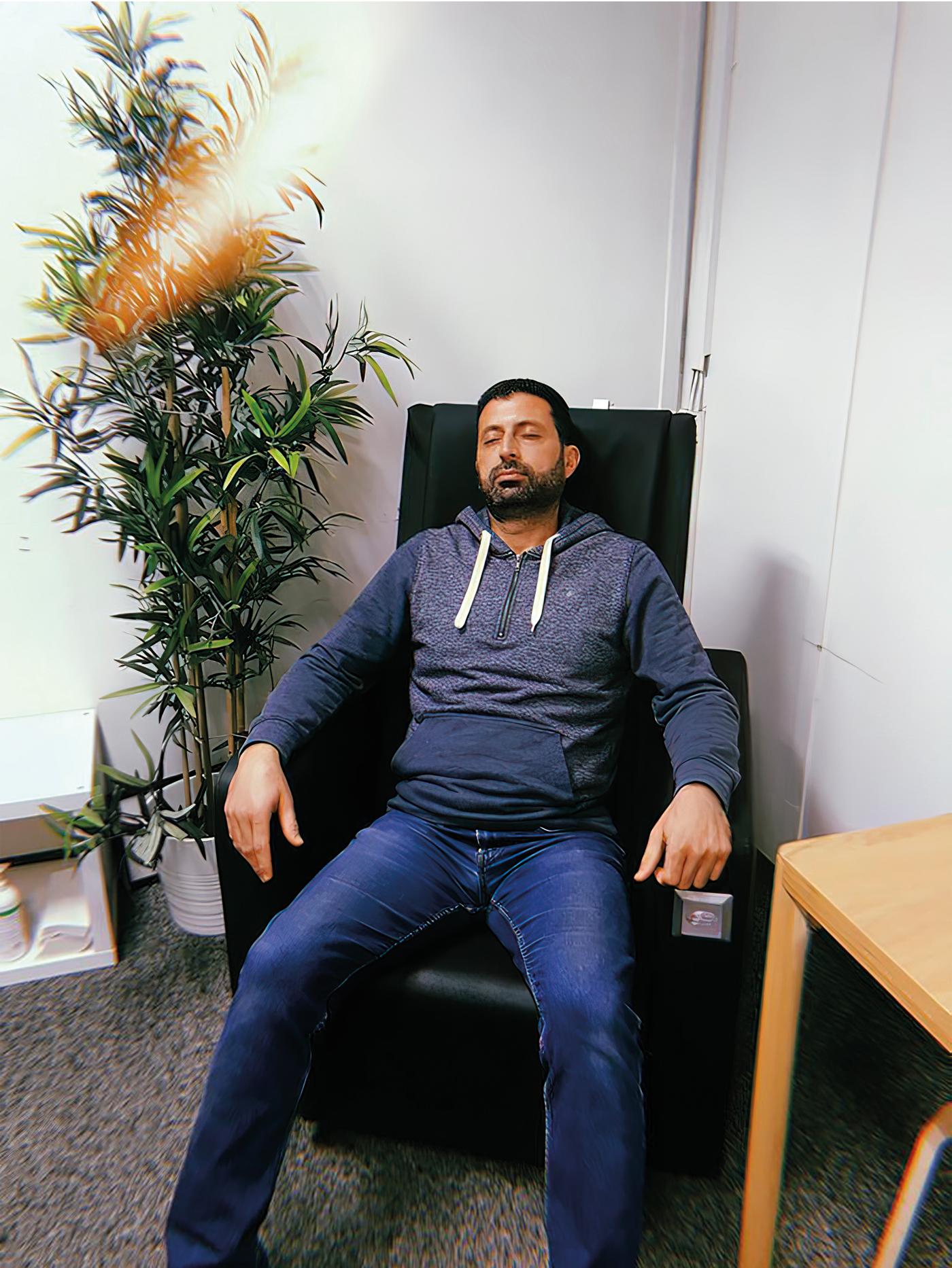 Odai, un rifugiato iracheno e co-worker IKEA, seduto su una sedia nera reclinata con indosso jeans e una felpa con cappuccio – IKEA.