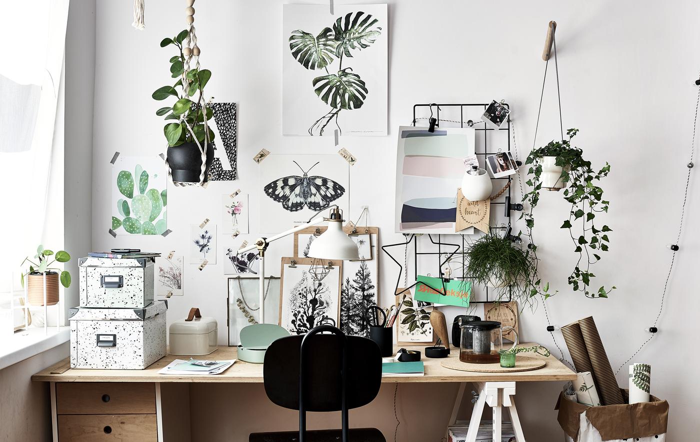 Œuvres d’art et inspiration sur un mur, au-dessus d’un bureau en bois complété par une chaise noire.
