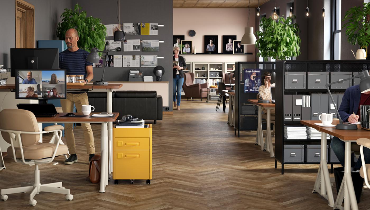 Office space with IDÅSEN beige sit-stand desks, swivel chairs and diverse office drawers with various people at work.