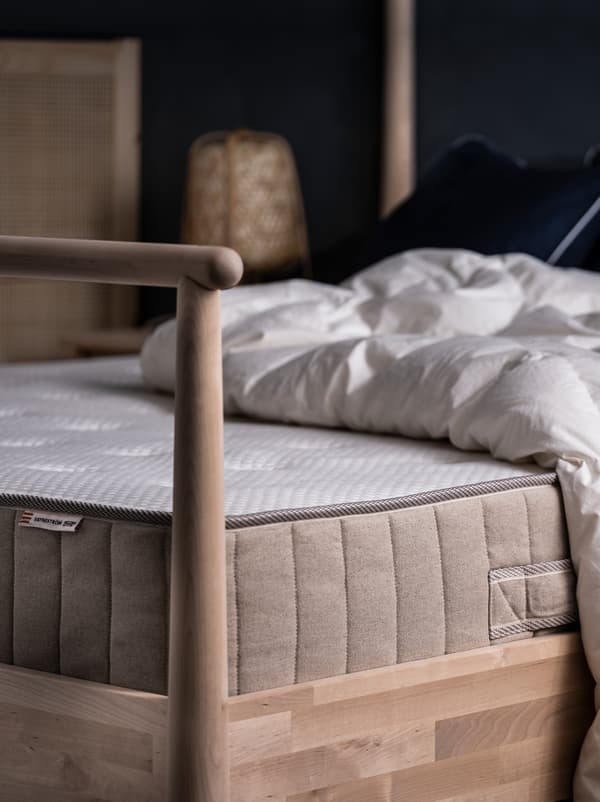On a GJÖRA birch bed in a softly lit bedroom lie a mattress and a duvet, both without additional bed linen.