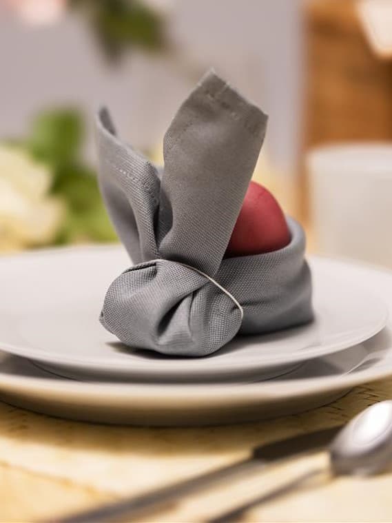 On a white plate sits a rabbit made from a napkin. The napkin has a circle at the back where you can place an egg.
