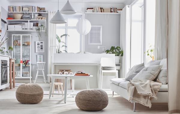 One-room apartment interior with a light colour scheme: bed, sofa, kitchenette, storage, and two SANDARED pouffes.