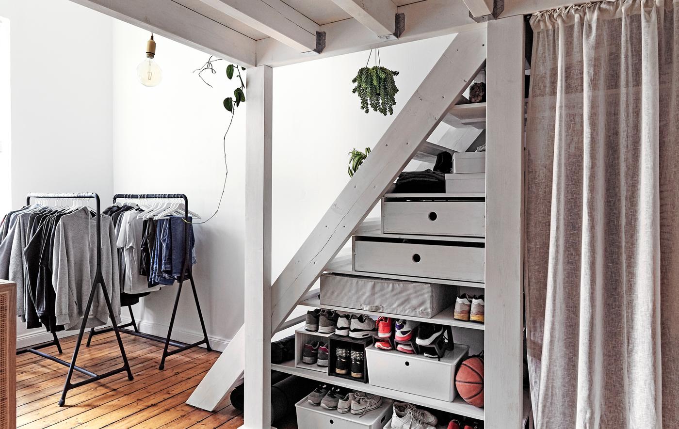 Open clothes rails and storage boxes under a flight of stairs.