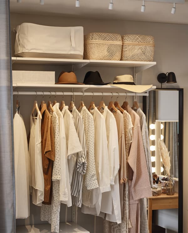 Open storage system with clothes that hang on a clothes rail. Storage cases, boxes and hats are stored on the shelves above.